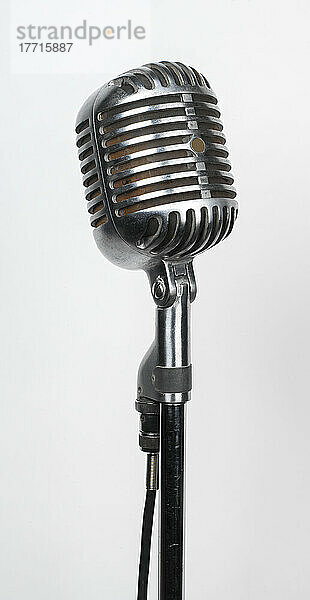 Nahaufnahme eines alten  verchromten Studiomikrofons auf einem Ständer vor einem weißen Hintergrund; Studioaufnahme