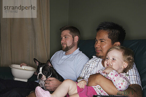 Homosexuelles Paar sitzt auf Couch mit Kind und Boston Terrier