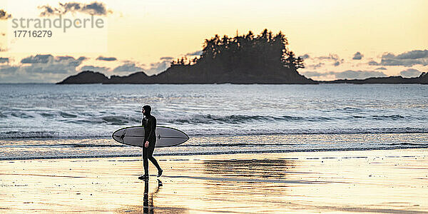 Ein Surfer trägt sein Surfbrett auf dem nassen Sand am beliebten Surfrevier am Chesterman Beach  Pacific Rim National Park Reserve  Vancouver Island; British Columbia  Kanada