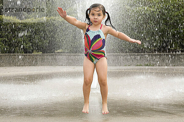 Junges asiatisch-weißes Mädchen springt und spielt in einem Wassersprinkler; Ontario Kanada