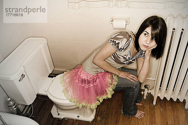 Junge Frau sitzt auf dem Rand der Toilette