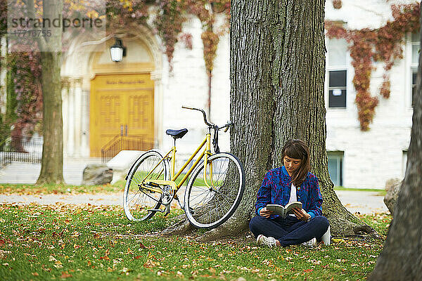 Mädchen liest Buch auf dem Universitätscampus im Herbst mit gelbem Fahrrad; Kingston  Ontario  Kanada