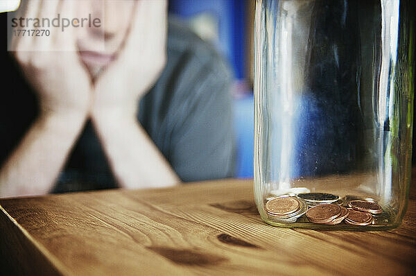 Mann mit Blick auf ein Einmachglas mit einer kleinen Menge von Münzen
