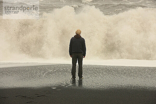 Mann  der vor großen Wellen an einem schwarzen Sandstrand in der Nähe von Vik  Island  steht