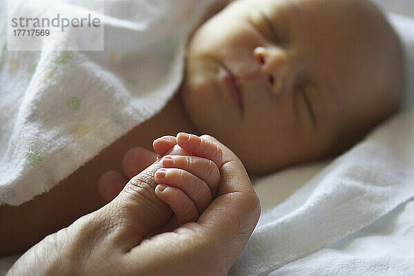 Erwachsene Hand  die die Hand eines neugeborenen Babyjungen hält