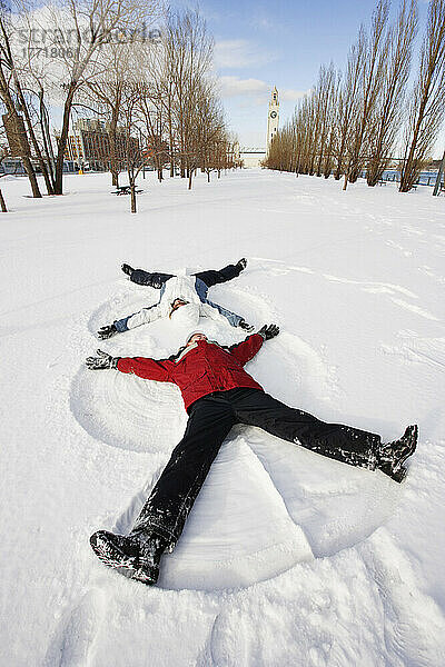 Mädchen machen Schneeengel mit Uhrenturm im Hintergrund