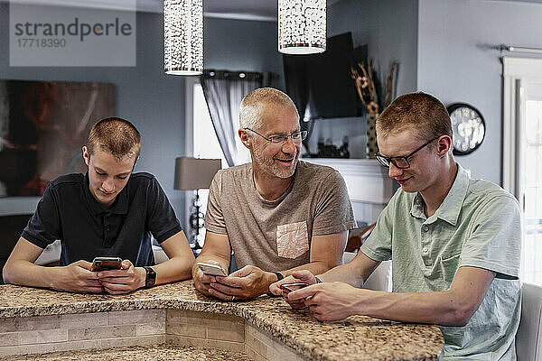 Vater und zwei Söhne sitzen zu Hause an der Kücheninsel und benutzen ihre Smartphones  wobei der Vater versucht  mit ihnen zu sprechen; Edmonton  Alberta  Kanada