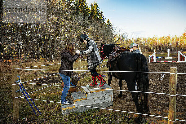 Ein junges Mädchen mit Cerebralparese steigt während einer Hippotherapie-Sitzung mit Hilfe ihrer Mutter und ihres Trainers von ihrem Pferd ab; Westlock  Alberta  Kanada