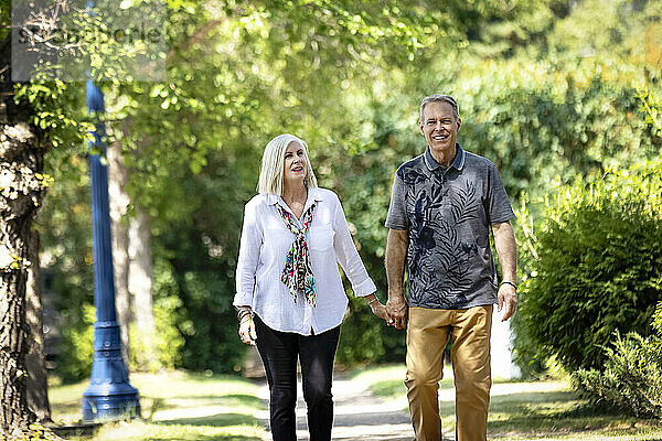 Älteres Paar hält sich an den Händen  während es im Freien auf einem Parkweg spazieren geht; Edmonton  Alberta  Kanada