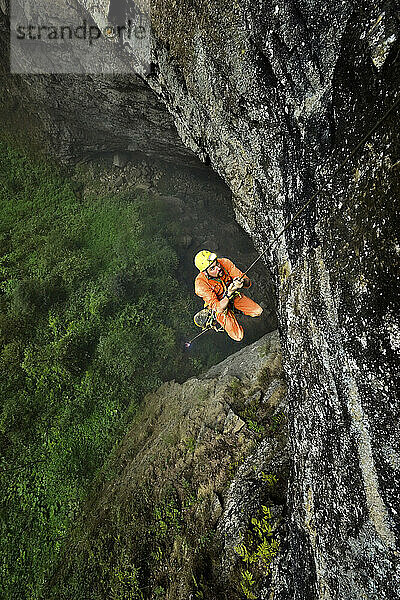 Ein Höhlenforscher klettert an einem dünnen Seil zu einem kleinen Vorsprung hinauf  von dem aus er die riesige Bodenfläche des Niubizi Tian Keng im Er Wang Dong-Höhlensystem überblickt.