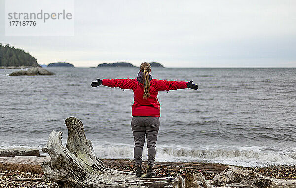 Frau steht am Ufer und blickt mit ausgestreckten Armen auf den Ozean  Sergeant Bay  Sunshine Coast; British Columbia  Kanada