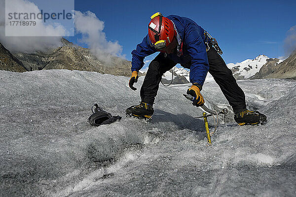 Ein Expeditionsleiter befestigt eine Eisschraube  um ein Seil zu verankern  bevor er in eine Gletschermühle hinabsteigt.