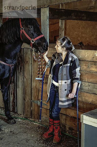 Ein junges Mädchen mit Cerebralparese mit einem Pferd in einer Scheune während einer Hippotherapie-Sitzung; Westlock  Alberta  Kanada