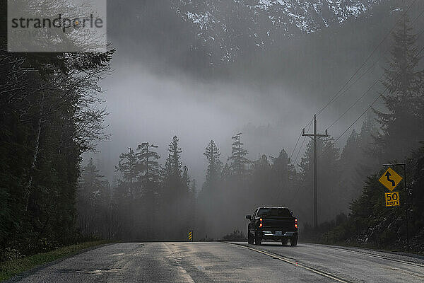 Ein Pickup fährt auf einer Straße in eine Nebelbank  die die Straße und den Wald vor ihm auf Vancouver Island verdeckt; Alberni-Clayoquot Regional District  British Columbia  Kanada