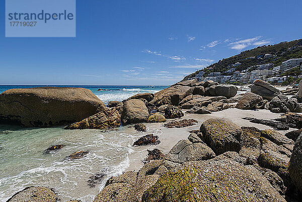 Große Felsbrocken entlang des felsigen Ufers mit Strandgebäuden am Hang von Clifton Beach; Kapstadt  Westkap  Südafrika