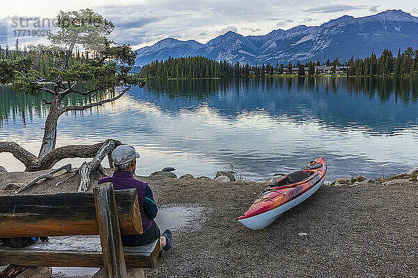 Frau auf Bank und Kajak am Ufer des Beauvert Lake im Jasper National Park mit der Fairmont Jasper Park Lodge im Hintergrund; Alberta  Kanada