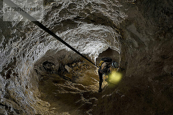 Ein Höhlenforscher sucht beim Klettern an einem Seil nach einem Halt.