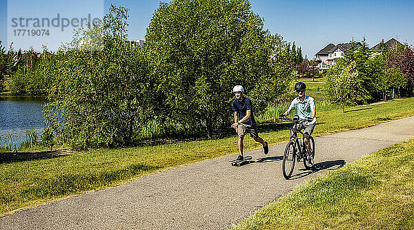 Brüder  die gemeinsam Zeit in der Nachbarschaft verbringen  einer auf einem Fahrrad und einer auf einem Skateboard; Edmonton  Alberta  Kanada