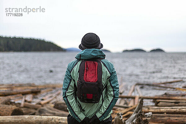 Person mit Hut und Rucksack steht und schaut auf den Ozean und die Küstenlinie  Sunshine Coast  BC  Kanada; British Columbia  Kanada