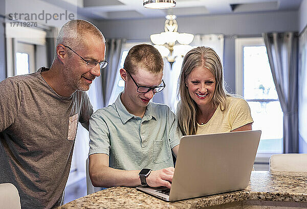 Junger Mann  der zu Hause einen Laptop benutzt  während seine Eltern zusehen; Edmonton  Alberta  Kanada