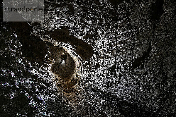 Ein Mitglied des Expeditionsteams steigt in die Veryovkina-Höhle hinab. Dies ist der Blick in die untere Hälfte der gleichen 55 m tiefen Grube. In der gesamten Eingangsserie weisen die Wände Anzeichen einer Bänderung innerhalb jeder Schicht auf. Auf diesem Foto sehen wir die perfekt geschliffenen  glatten Wände  die im Laufe der Zeit durch die Einwirkung von Wasser erodiert wurden; Gagra  Kaukasus  Abchasien