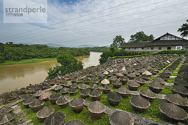 Sojasaucenfabrik mit traditionellen Sojasaucengläsern am Flussufer  die unter den für die Herstellung von Sojasaucen idealen Bedingungen von Sonne und feuchter Luft im südlichen Sichaun  Sichuan  China  natürlich gären