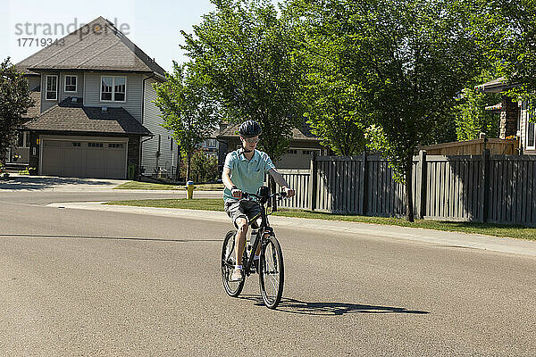 Junger Mann fährt mit dem Fahrrad eine Wohnstraße entlang; Edmonton  Alberta  Kanada