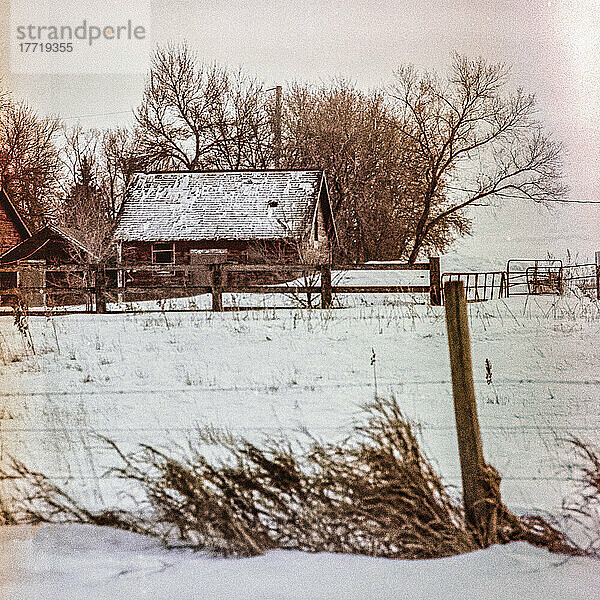 Altes Gehöft an einem Wintertag  mit schneebedeckten Gebäuden und einem eingezäunten Feld im Vordergund