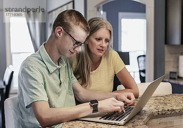 Junger Mann benutzt zu Hause einen Laptop mit Unterstützung seiner Mutter; Edmonton  Alberta  Kanada