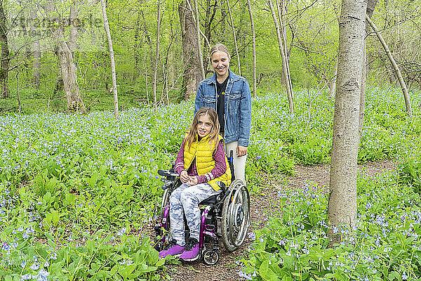 Mädchen im Rollstuhl und ihre Freundin posieren im Waldgebiet beim Betrachten von Wildblumen am Potomac River; Cabin John  Maryland  Vereinigte Staaten von Amerika