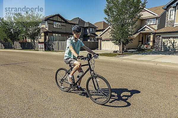 Junger Mann fährt mit dem Fahrrad eine Wohnstraße entlang; Edmonton  Alberta  Kanada