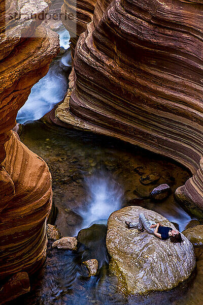 Ein Wanderer entspannt sich auf einem großen Felsen in einem Slot Canyon am Colorado River bei Meile 136 in den Arizona Cascades entlang des Deer Creek; Grand Canyon National Park  Arizona  Vereinigte Staaten von Amerika