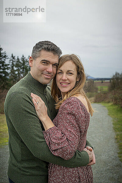 Mittleres erwachsenes Paar steht im Freien in einem Park in einer spielerischen  zärtlichen Umarmung; Aldergrove  British Columbia  Kanada