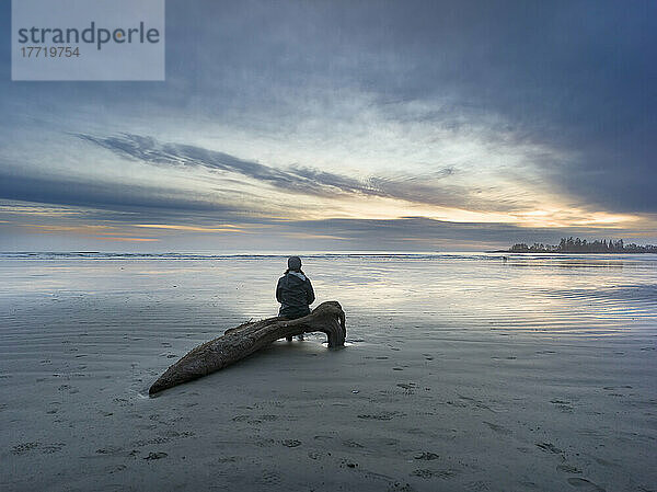 Eine Frau sitzt auf Treibholz und genießt den Sonnenuntergang am Long Beach  dem größten und längsten Strand im Pacific Rim National Park Reserve an der Westküste von Vancouver Island; British Columbia  Kanada