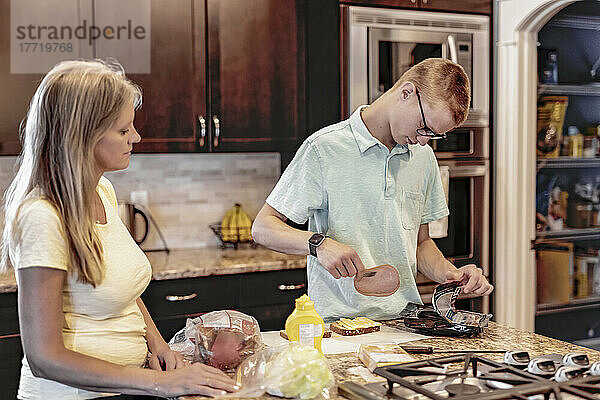 Junger Mann bereitet zu Hause in der Küche das Mittagessen zu  während seine Mutter zusieht und ihn unterstützt; Edmonton  Alberta  Kanada