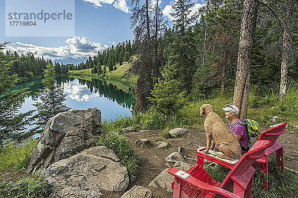 Eine ältere Frau und ihr Hund genießen die beiden roten Adirondack-Stühle im Valley of the Five Lakes im Jasper National Park; Alberta  Kanada