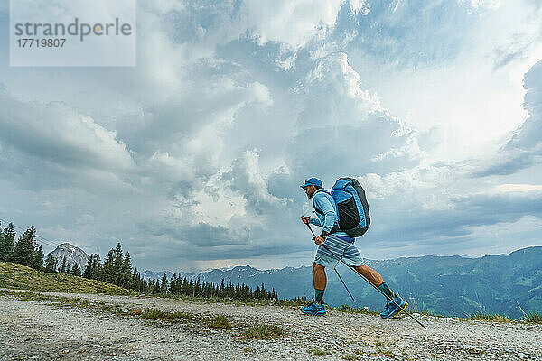 Ein Athlet des Redbull X Alps  eines Gleitschirmrennens  wandert entschlossen den Bergpfad entlang zu einem Gipfel  um seinen Gleitschirm unter einem stürmischen Himmel zu starten; Wagrain  Salzburgerland  Österreich