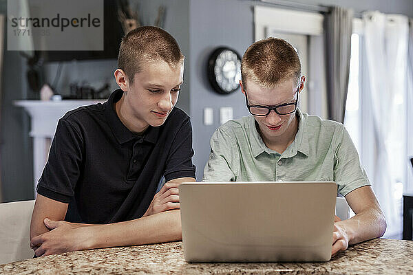Ein junger Mann benutzt zu Hause einen Laptop  während sein Bruder den Bildschirm neben ihm beobachtet; Edmonton  Alberta  Kanada