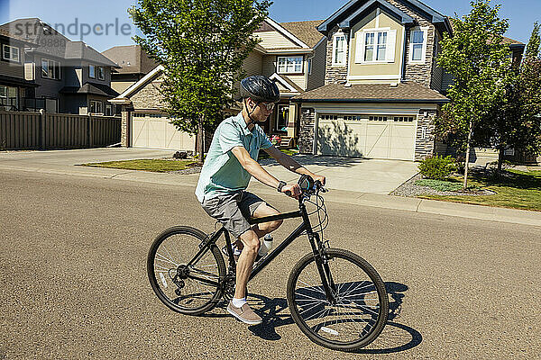 Junger Mann fährt mit dem Fahrrad eine Wohnstraße entlang; Edmonton  Alberta  Kanada