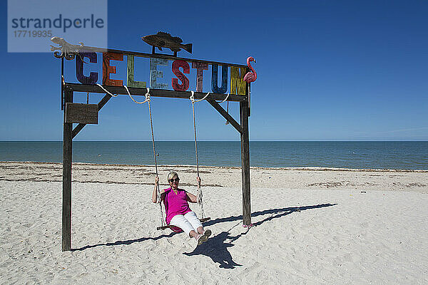 Frau auf einer Schaukel mit Celestun-Schild an einem weißen Sandstrand an der Küste des Golfs von Mexiko; Celestun  Bundesstaat Yucatan  Mexiko