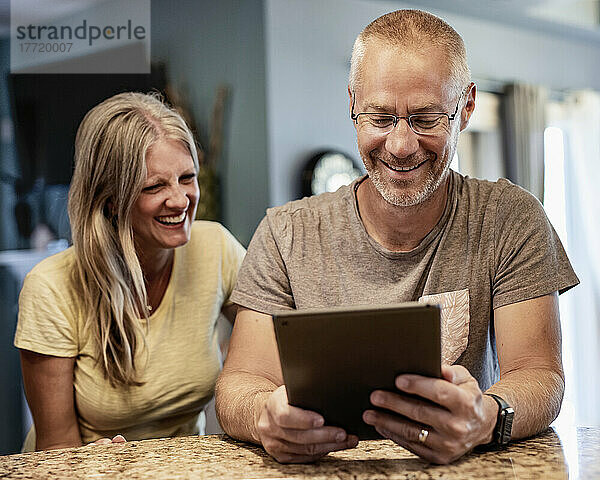 Älteres Paar  das zu Hause sitzt und gemeinsam über Inhalte auf einem Tablet lacht; Edmonton  Alberta  Kanada