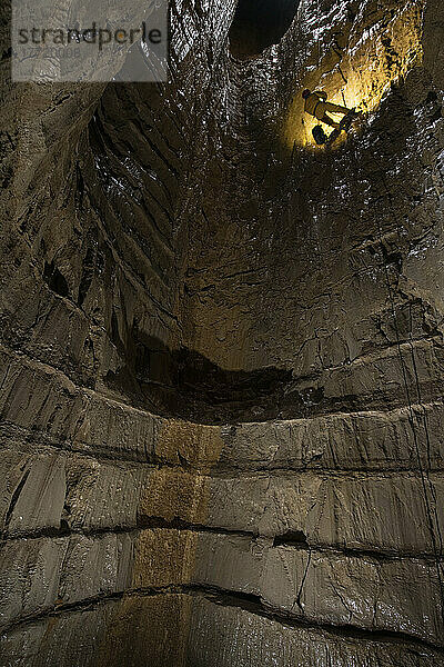 Ein Mitglied des Expeditionsteams arbeitet sich an den Seilen hinunter in den unteren Teil dieses beeindruckend aussehenden Schachts. Von der Sohle desselben 55 m tiefen Schachts ist der Blick nach oben ebenso beeindruckend  da er die horizontale Bänderung innerhalb der Schichtebenen gut erkennen lässt; Gagra  Kaukasusgebirge  Abchasien
