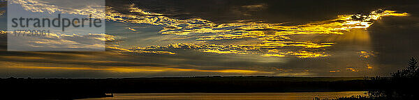 Panorama eines dramatischen  farbenfrohen Himmels mit vom Himmel herabfallenden Sonnenstrahlen  die sich auf einem See mit silhouettierten Hügeln spiegeln; Calgary  Alberta  Kanada