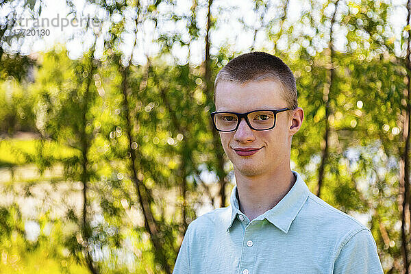 Porträt eines jungen Mannes im Freien mit Baumblättern und Wasser im Hintergrund; Edmonton  Alberta  Kanada