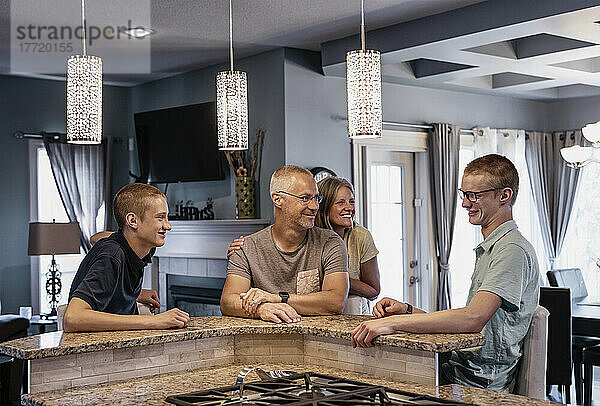 Vater und Mutter mit zwei Söhnen sitzen zu Hause an der Kücheninsel und reden miteinander; Edmonton  Alberta  Kanada