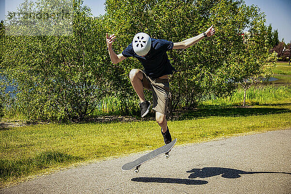 Junger Mann auf einem Parkweg mit einem Skateboard  der einen Flip-Trick macht; Edmonton  Alberta  Kanada