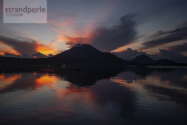 Dramatische Schönheit des Spiegelbilds des Vulkans Tavurvur und glühende Wolken bei Sonnenaufgang im ruhigen Ozeanwasser; Neubritannien  Papua-Neuguinea