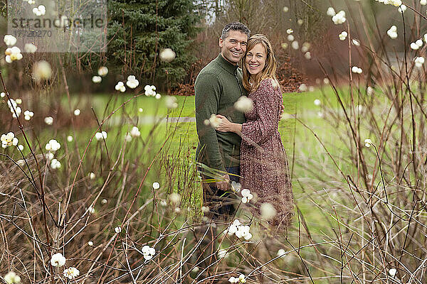 Ein erwachsenes Paar steht im Freien in einem Park und umarmt sich liebevoll  mit Blüten im Vordergrund; Aldergrove  British Columbia  Kanada