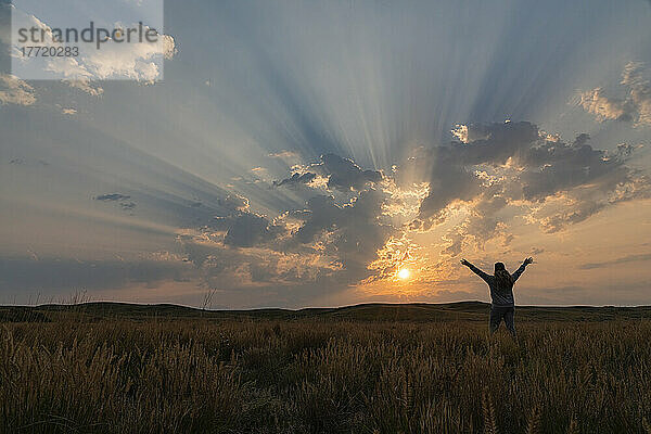 Korpuskulare Strahlen bei Sonnenaufgang über der Prärie von Saskatchewan. Frau steht und freut sich über die Schönheit eines neuen Tages; Saskatchewan  Kanada