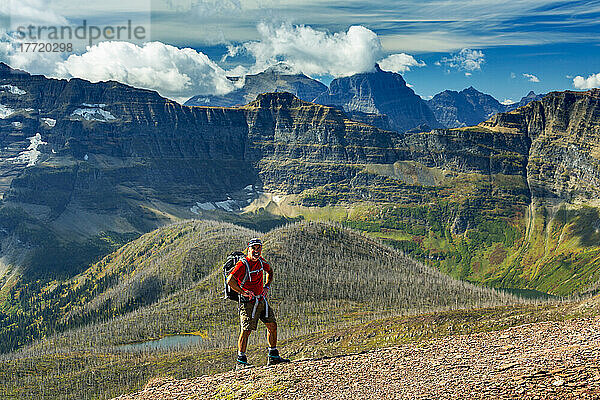 Männlicher Wanderer auf dem Gipfel eines Bergrückens mit Blick auf das darunter liegende Tal und die Bergketten im Hintergrund mit blauem Himmel und Wolken  Waterton Lakes National Park; Alberta  Kanada